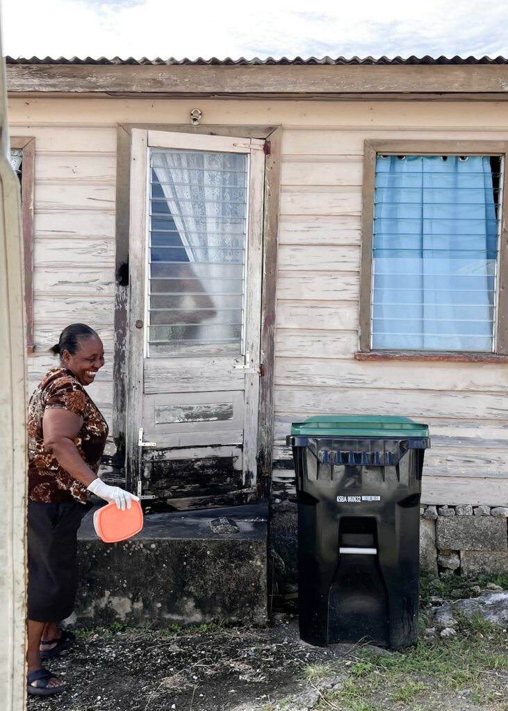 Image of a woman smiling as she delivers a tupperware container of food to a house.