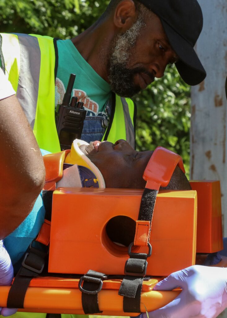 Image of a man applying neck brace equipment to another man in a training simulation.