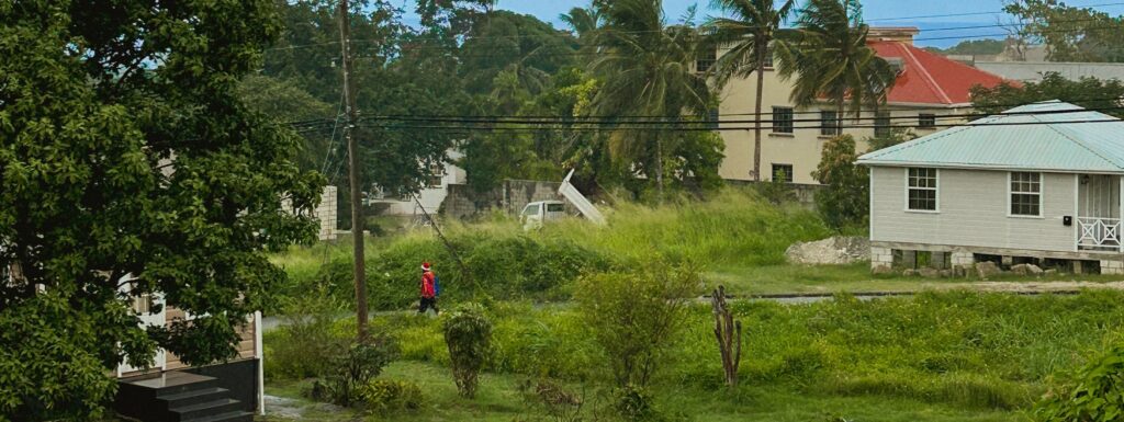 Image of a Barbados landscape, with a single man in red walking down the street in the middle ground.